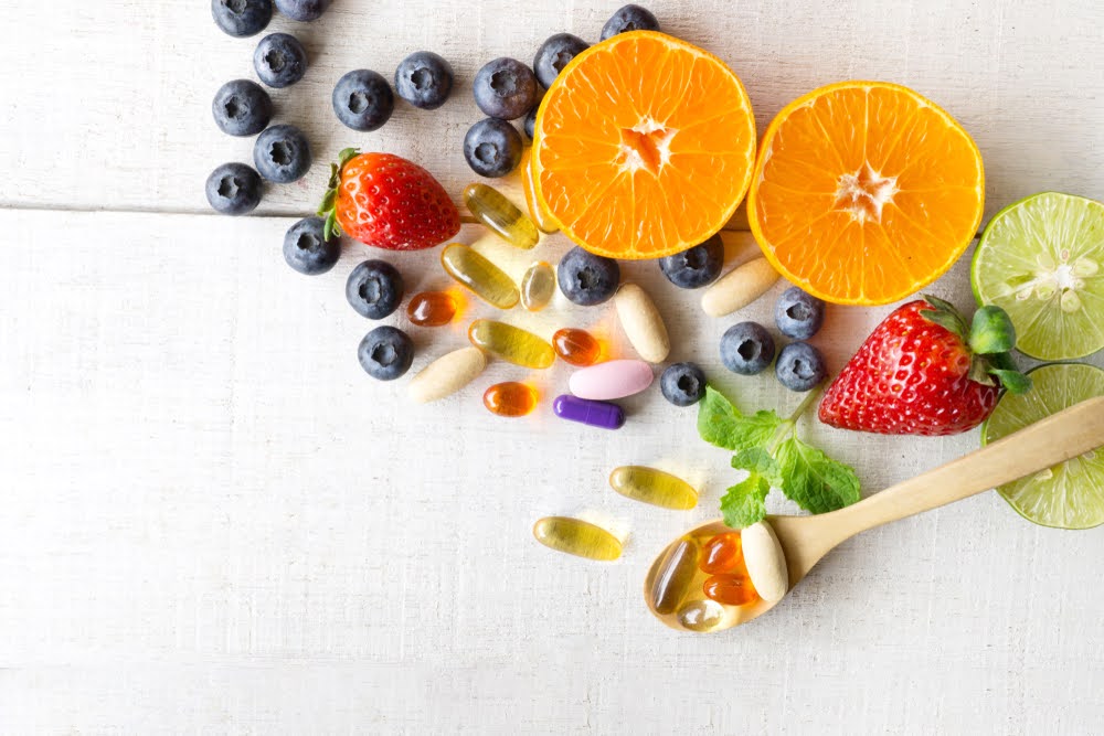 selection of vitamin capsules and fruits on a white linen counter