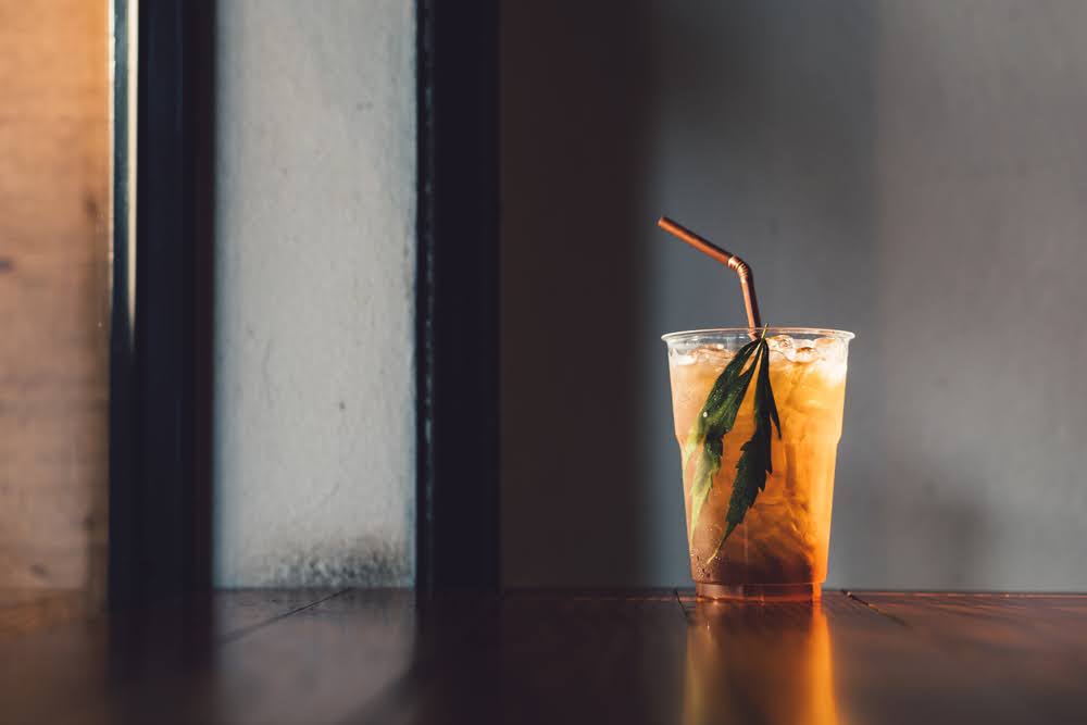 THC infused tea on a wooden table in a clear cup with a straw