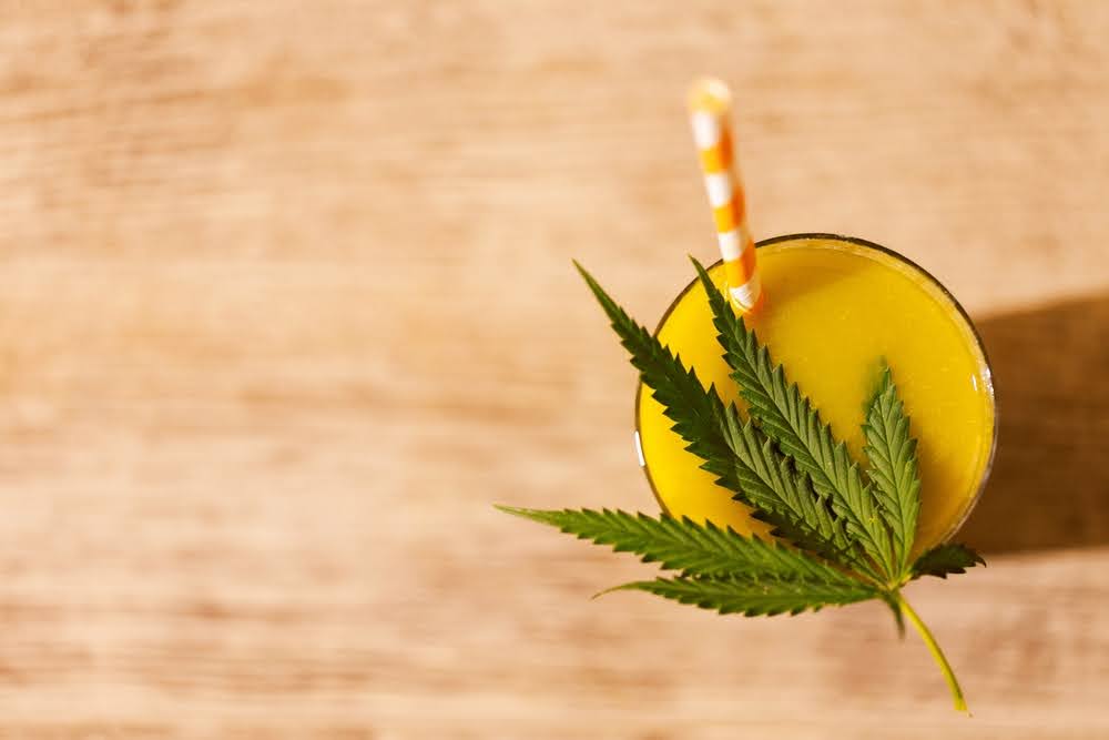 overhead shot of a glass of orange juice with a hemp leaf on top