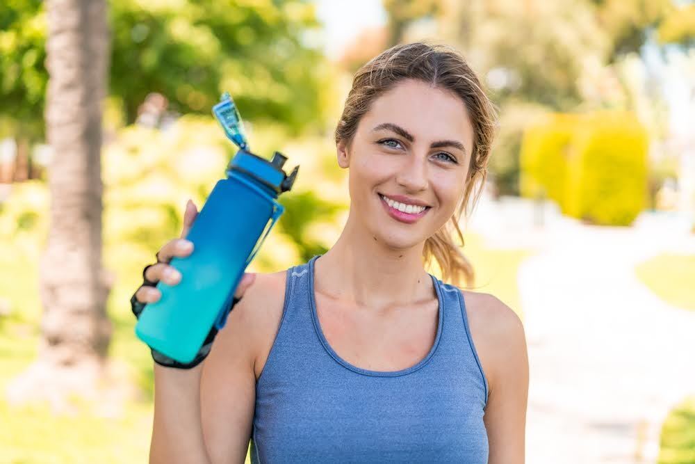 woman in fitness attire looking at the camera and holding a water bottle