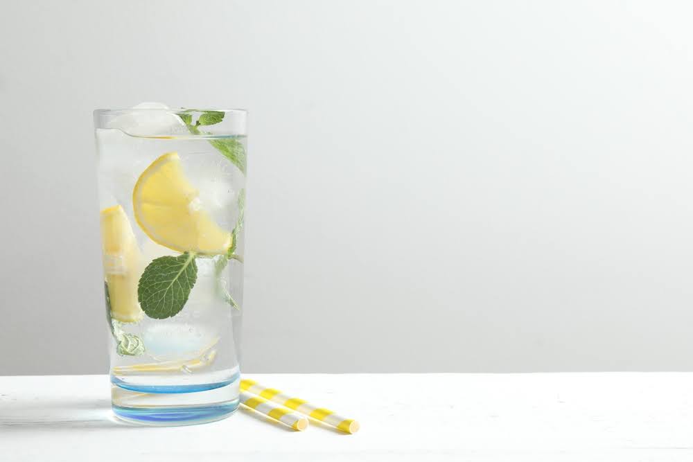 sparkling social tonic in a clear glass with a lemon wedge and mint on a white counter