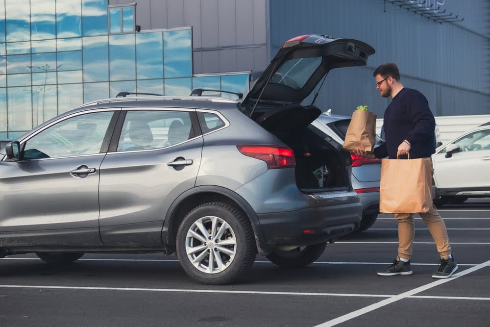 man putting brown paper bags into the trunk of his car