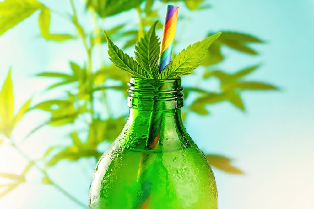 closeup of green bottle with hemp leaf and rainbow straw with a blue sky backdrop