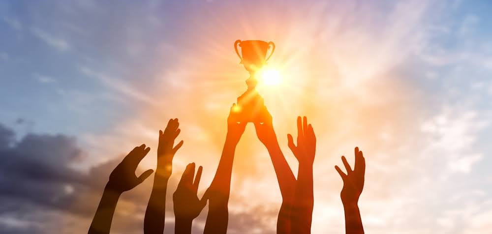 hands in the air lifting up a trophy against a sunset background