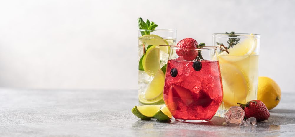 lemon, lime and strawberry mixed drinks in clear white glasses on a light gray counter