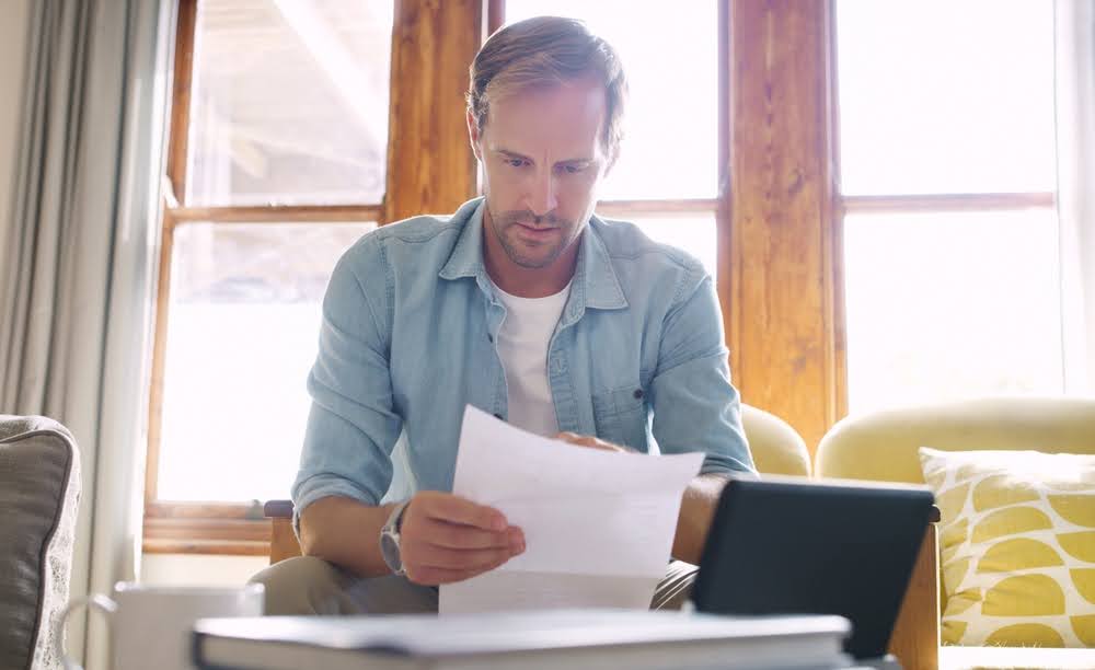 man sitting on a couch reading a single piece of paper