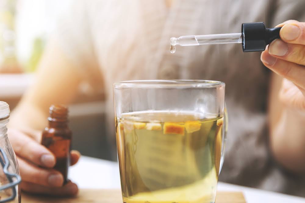 closeup of a person adding a tincture droplet into a tea
