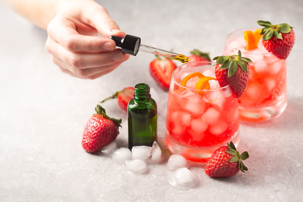 mixed cocktails with strawberries on a counter and a hand holding a tincture over them