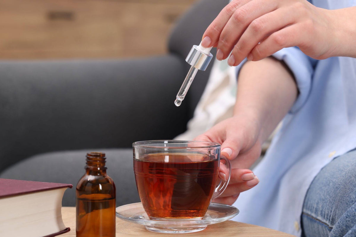 close-up of a hand using a tincture to add a liquid to their tea