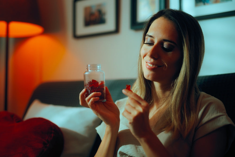 woman sitting on a couch holding a bottle of red cbd gummies