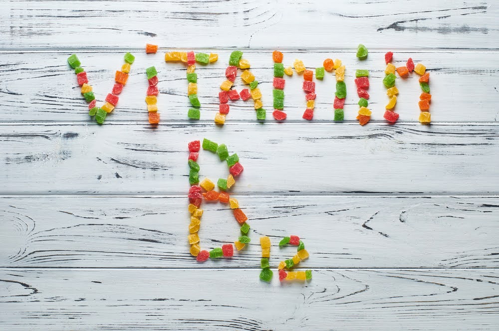 the words vitamin b12 written in colorful gummies on a white painted wooden panel
