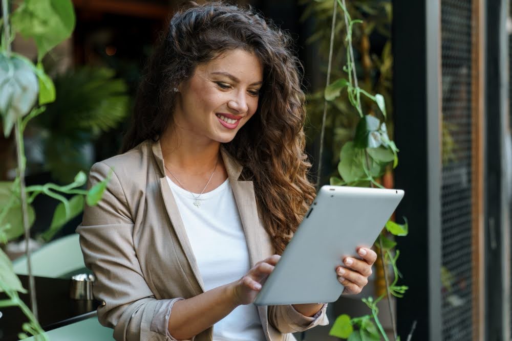 woman standing next to hanging plants and browsing on a personal tablet